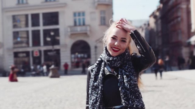 Rotation view of a young attractive blonde girl with red lipsticks, and casual leather jacket having a walk in the center of an ancient city. Happy mood. Sunny day, time to be happy.