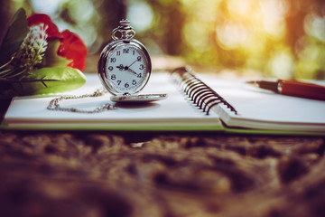 pen, packet watch and rose  on the desk, open a blank white notebook on table