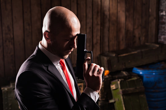 Contract assassin in suit and red tie holds gun