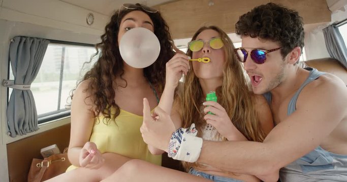 Portrait Beautiful Teenage hipster friends blowing bubblegum candy bubbles having fun at festival in camper van on road trip adventure