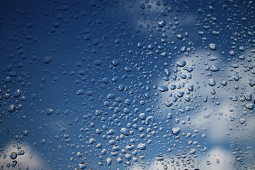 Rain drops on window with blue cloudy sky in background , spring rainy day 