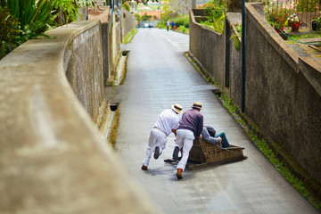 Toboggan riders pushing wooden sledge downhill in Funchal, Madeira island, Portugal