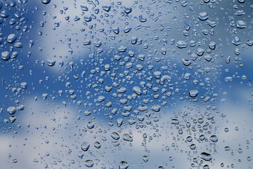 Rain drops on window with blue cloudy sky in background , spring rainy day 