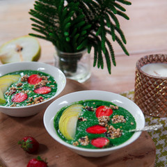 Healthy vegan food concept: green smoothie bowl with spinach, spirulina, pear and red strawberry topped with raw superfood granola. Vegetarian bright breakfast.