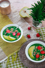 Healthy vegan food concept: green smoothie bowl with spinach, spirulina, pear and red strawberry topped with raw superfood granola. Vegetarian bright breakfast.