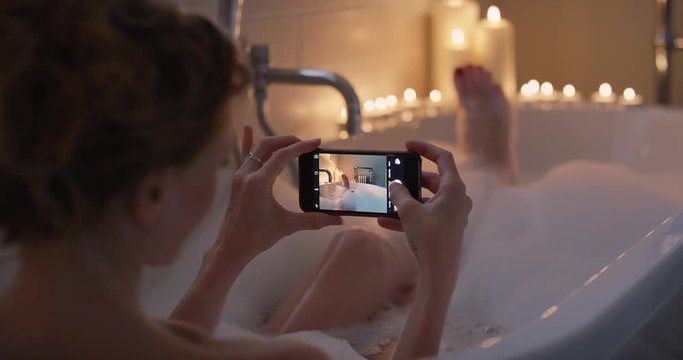 Sexy Woman lying in bubble bath taking photos of feet using smartphone sharing  on social media relaxing at home mindfulness concept