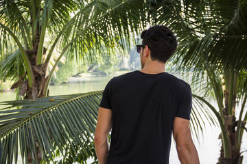 Back of young man outdoor in nature, near palm trees in a sunny day