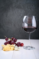 A glass of red wine, a bunch of grapes and cheese on the table