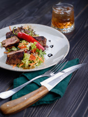 Tagliata of beef with salad on a white plate and a glass of whiskey