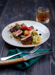 Tagliata of beef with salad on a white plate and a glass of whiskey