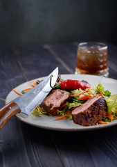 Tagliata of beef with salad on a white plate and a glass of whiskey