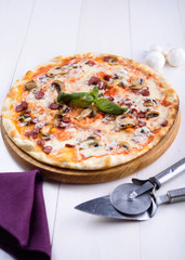 Pizza with mushrooms and sausages on a wooden board next to the devices for pizza