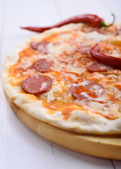 Pizza with salami, pepper and tomato sauce on a wooden board