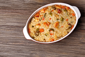 Baking dish with delicious rice and chicken on wooden table