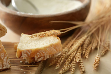 Tasty bread, wooden board and wheat spikelets on kitchen table