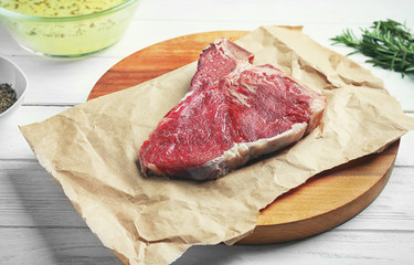 Parchment with fresh raw steak on wooden board