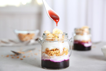 Pouring jam onto delicious dessert in glass jar