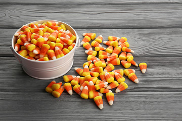 Bucket with tasty Halloween candies on wooden background