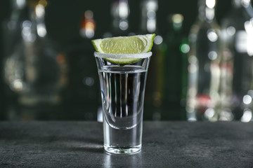 Tequila shot with juicy lime slice and salt on blurred background of glass bottles
