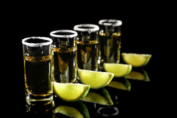 Row of golden tequila shots with juicy lime wedges and salt on black background