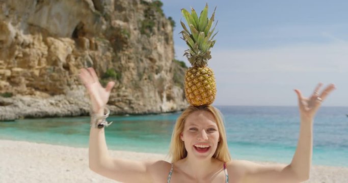 Happy woman balancing pineapple on head posing for camera being silly and playful on tropical beach summer vacation holiday