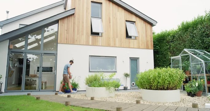Man plants and waters seedlings in home garden in slow motion outdoors in front of new modern home