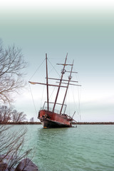 Rusty shipwreck with tall masts in a cover near shore, dark stormy sky above