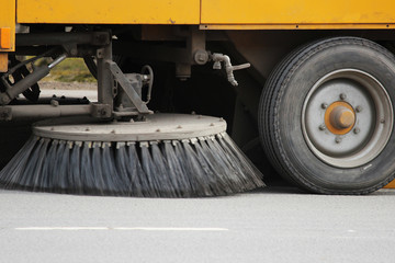 Yellow urban sweeper cleans road from dirt with a round brush in the spring.