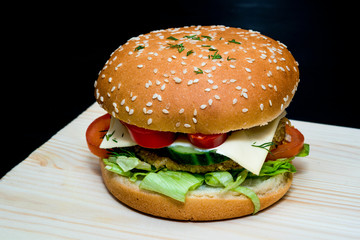 Hamburger with pepper, cheese, cucumber,sesame and greens on a wooden board