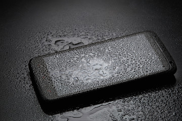 Smartphone with water drops on dark background
