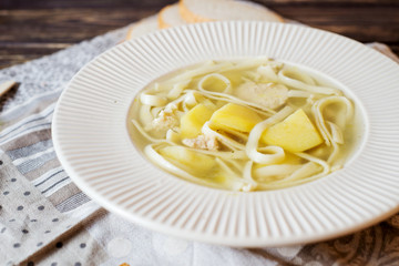 Useful, hearty and healthy lunch, chicken soup with homemade noodles, potatoes, spices and white fresh bread on a wooden background 