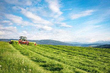 Mähen einer Wiese für Silage mit Alpen im Hintergrund