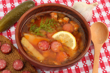 saltwort russian beef, pork and sausage soup solyanka with lemon, salami in plate on red cloth