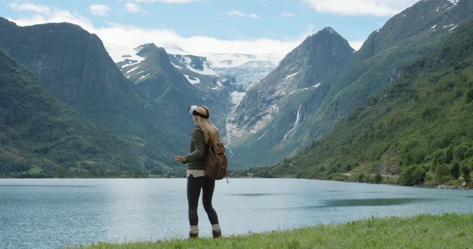 Brave woman hiker traveler looking at Glacier Norway wearing virtual reality headset enjoying outdoor travel experience  watching 360 video climate change imagination concept