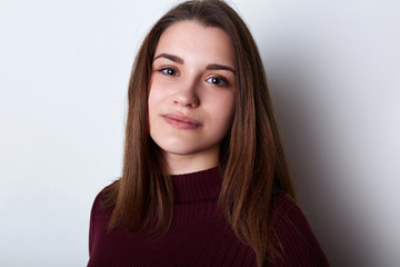 Fototapeta premium A portrait of beautiful brunette female with brown eys and charming lips having pleasant face dressed in casual sweater posing into camera while standing over white background. Beauty concept.