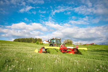 Schlepper mit modernem Mähwerk beim Gras mähen im Allgäu