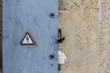 electrical hazard sign placed on a  locked electric power dashboard on a scratched painted wall