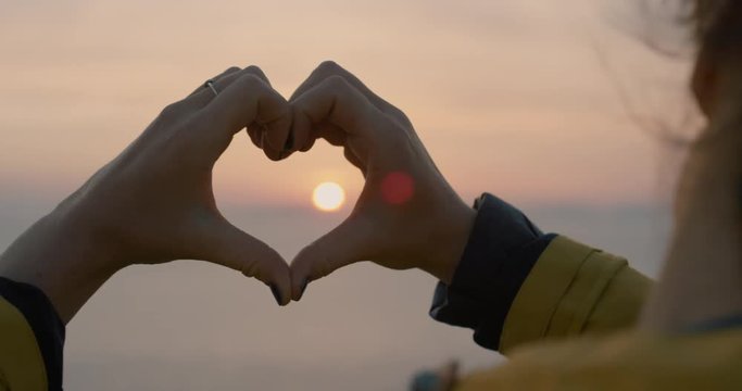 Beautiful Woman making heart shape with hands at sunset Girl holding up love symbol gesture with orange sun flare