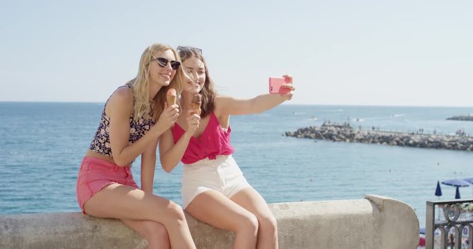 Young women taking selfie photo eating ice cream on beach Best friends sharing Italian Gelato outdoors in summer sunshine Girls enjoying European vacation travel adventure Amalfi Coast  Italy