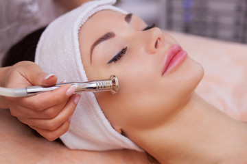 The doctor-cosmetologist makes the procedure Microdermabrasion of the facial skin of a beautiful,...