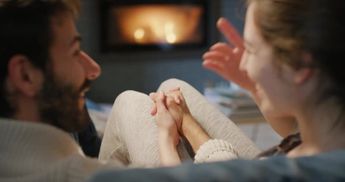 Romantic couple by the Cozy Fireplace. Man and Woman relax by warm fire and warming up their feet. Close up. Winter and Christmas holidays Hygge concept