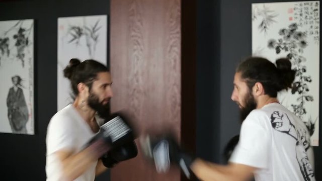 The twin brothers in boxing gloves sparring in the training hall. Chinese martial arts.