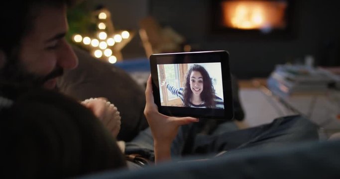 Young couple having video chat at home in front of fireplace holding smartphone webcam chatting to friend