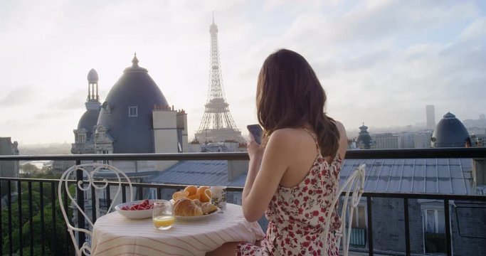 Travel woman taking photograph of Eiffel Tower Paris with smart phone sharing social media view from hotel terrace breakfast vacation