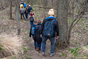 Group of friends walking with backpacks in spring forest from back. Backpackers hiking in the woods. Adventure, travel, tourism, active rest, hike and people friendship concept.