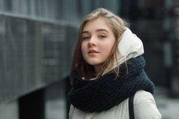 City portrait of young beautiful blonde stylish girl posing in spring fall outdoors in white coat black knitted scarf. Vintage filter film saturated colors. Emotion demonstration concept.