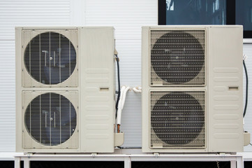 Close-up photo of two outdoor units of air conditioners standing on the ground in front of facade of the modern building