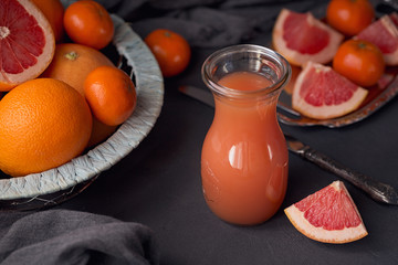 Glass of freshly squeezed grapefruit juice with fresh citrus fruits on dark background.
