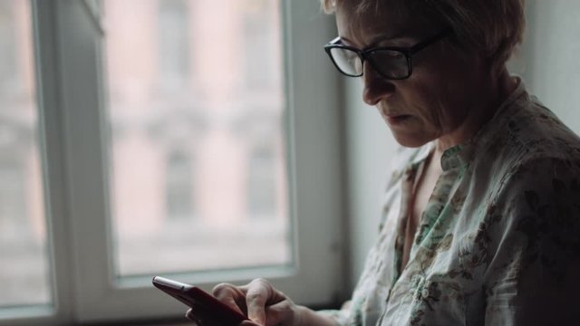 Side view shot of adult woman in glasses watching something on the smartphone screen