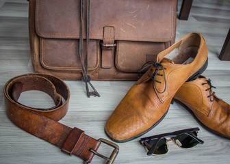 leather lifestyle with brown leather bag on wooden floor with leather dress shoes, sunglasses and suspenders for professional entrepreneur who is powerful yet stylish. background copyspace for company